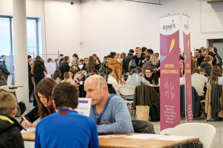 Des jeunes marchent dans la salle à travers les stands et d'autres sont assis face à nos exposants.